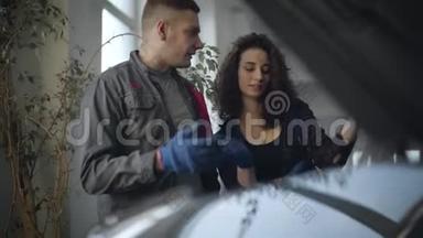 年轻男女工人在<strong>服务站</strong>讨论汽车修理。 专业的男人和女人在面前说话